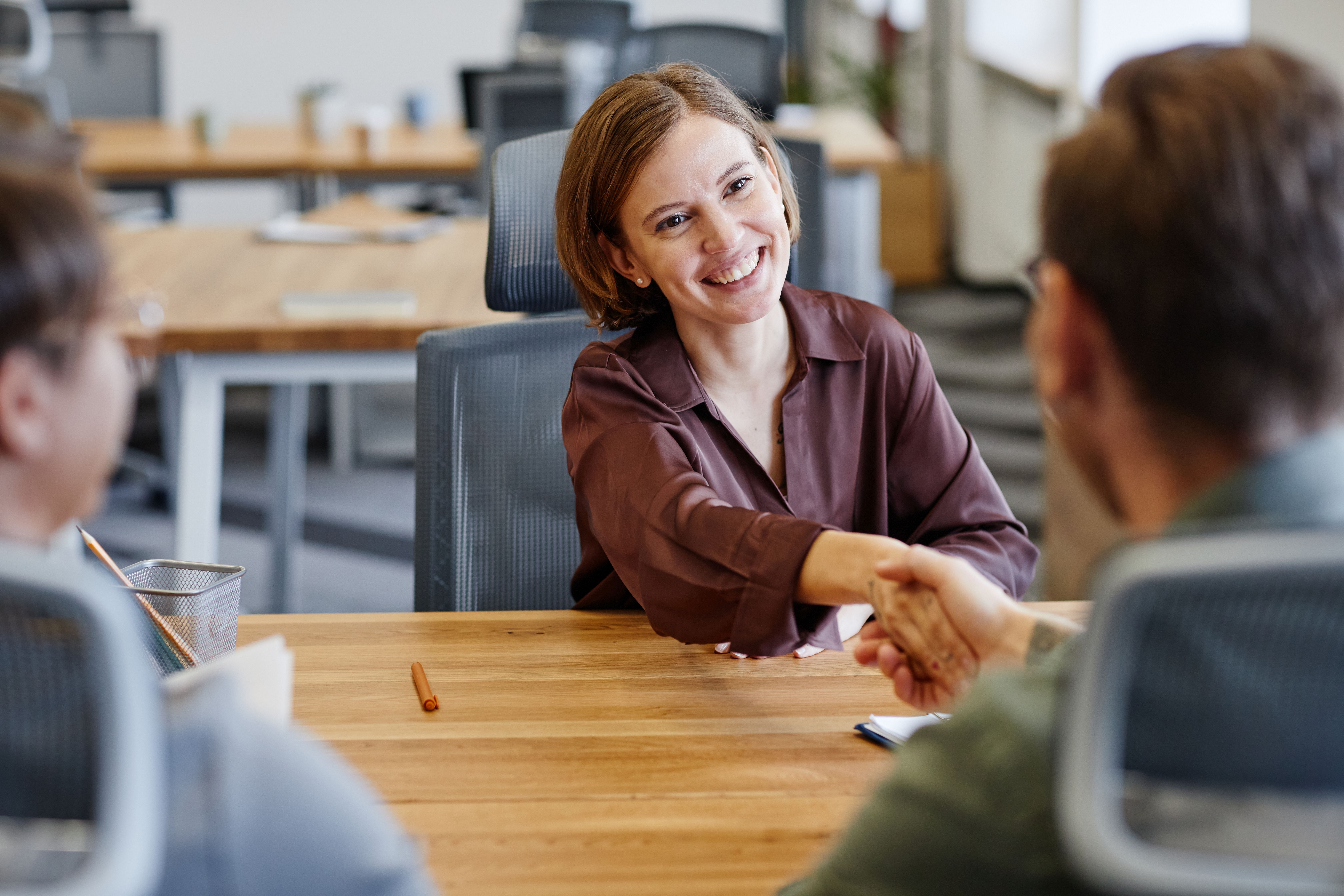 Portrait of smiling young woman shaking hands with HR manager at job interview in office, copy space